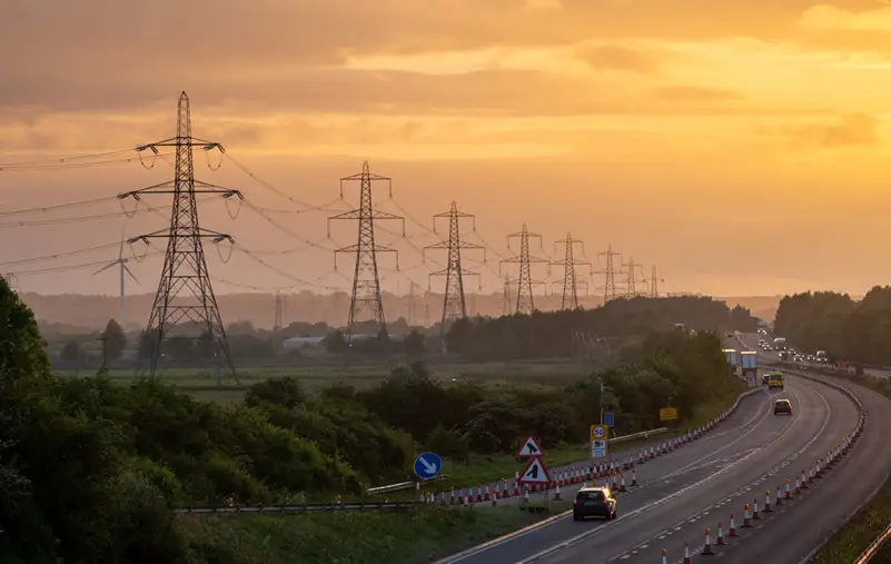 A line of pylons along a motorway at sunset